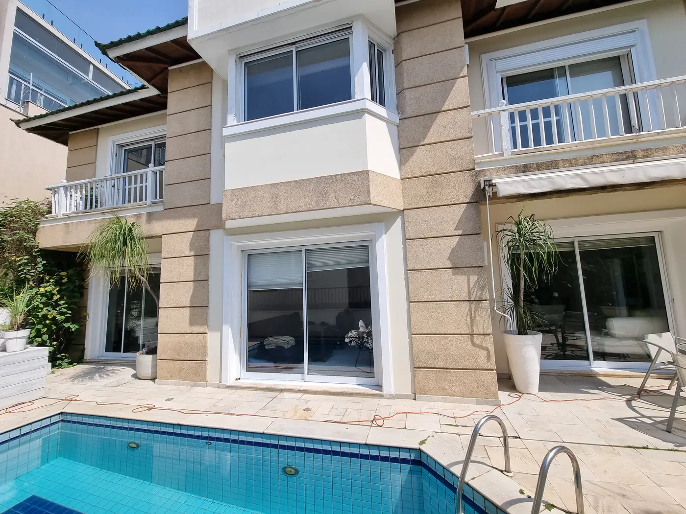 Fachada residencial com janelas e portas de correr brancas de alumínio ao lado da piscina